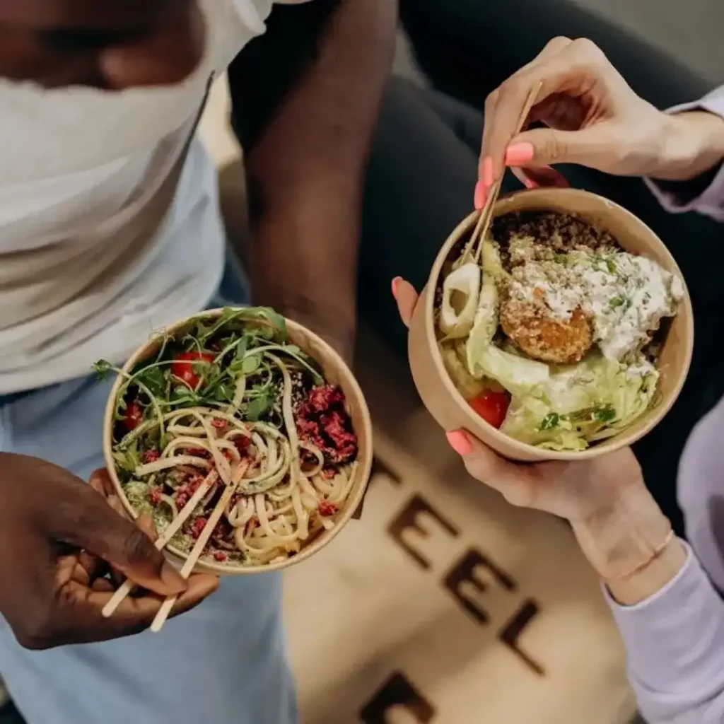 A man and woman sitting at a dining table sharing a colorful plant-based meal with vegetables, grains, and salads