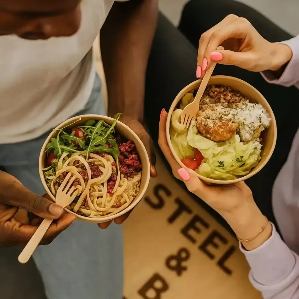 A man and woman sitting at a dining table sharing a colorful plant-based meal with vegetables, grains, and salads